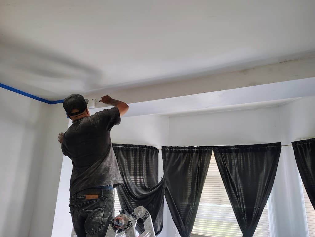 Technician on a ladder finishing ceiling trim work near a bay window